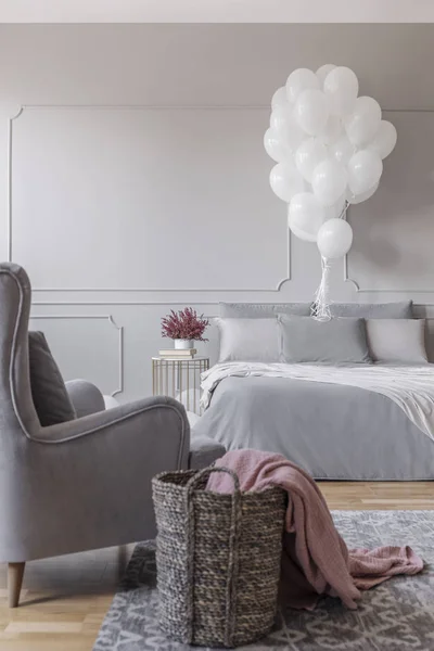 快適なベッド トレンディな肘掛け椅子 バスケット ピンクの毛布 空の壁にコピー スペースを実際の写真でグレーのスタイリッシュな寝室で誕生日の装飾 — ストック写真