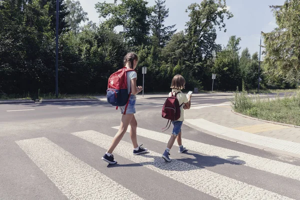 带着背包走过人行横道到学校的女孩和男孩 — 图库照片