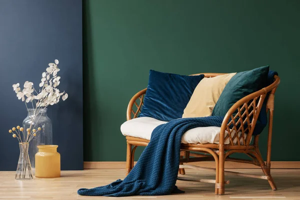 玻璃花瓶与鲜花旁边舒适的藤架与蓝色 祖母绿和米色枕头和毯子 真正的照片与复制空间在空的绿色墙 — 图库照片