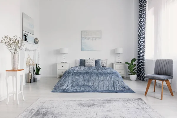 Mavi beyaz yatak odası iç posterler ve dolapları üzerinde lambalar ile yatakta yanındaki gri sandalye. Gerçek fotoğraf