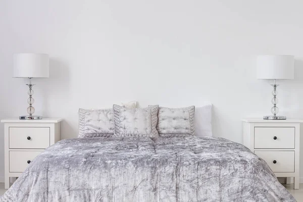 灰色床上用品在国王大小的床在时尚明亮的卧室内部与白色床头柜和灯 真正的照片与复制空间在空的白色墙壁 — 图库照片