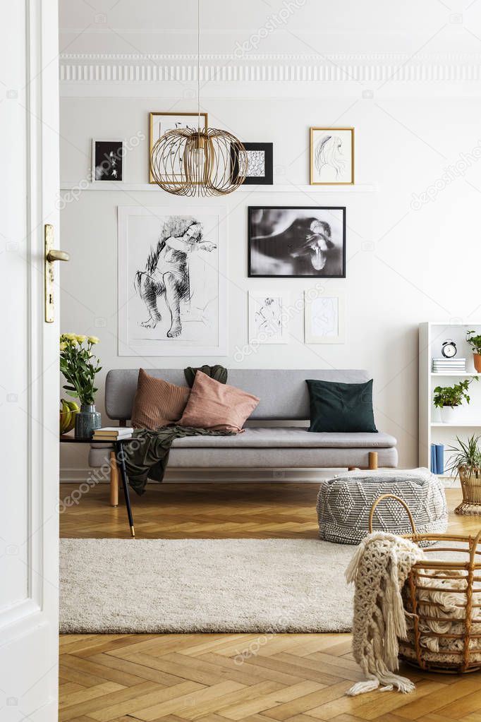 Blanket in basket next to carpet in living room interior with posters above grey settee. Real photo