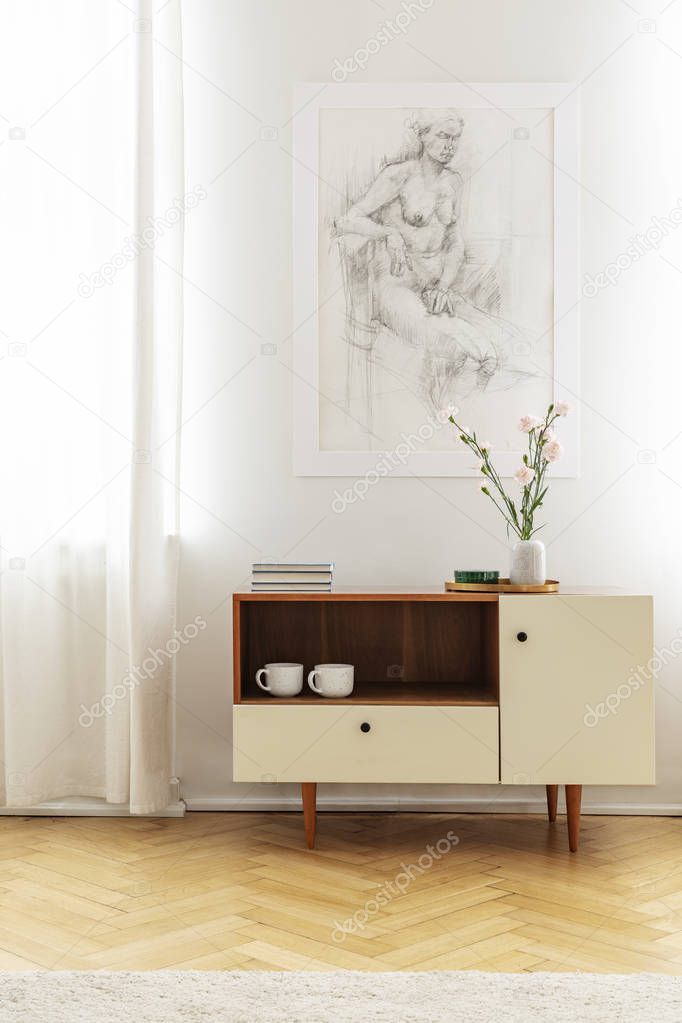 Poster on white wall above wooden cabinet with flowers in simple living room interior. Real photo