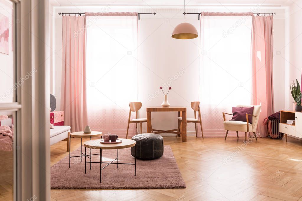 Dining table with chair in the middle of bright pastel pink living room in tenement house