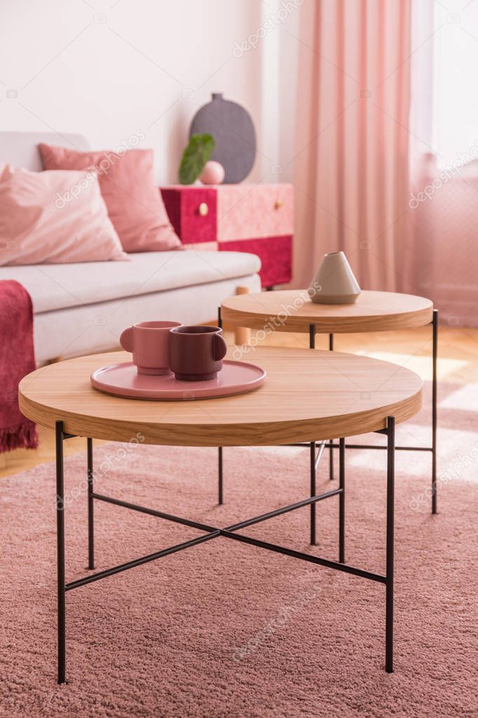 Pastel pink and burgundy coffee cups on the wooden coffee table in colorful living room interior