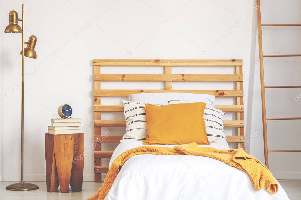 Yellow pillow and blanket on white wooden single bed in natural bedroom, real photo