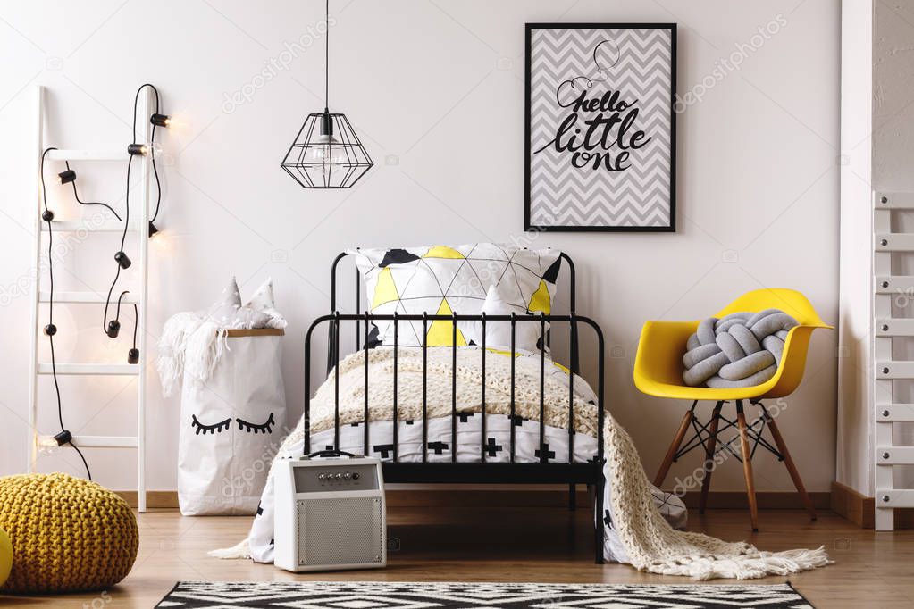 Trendy yellow chair with grey knot pillow next to industrial metal bed in black and white bedroom with Scandinavian design