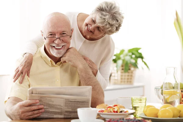 Lyckliga Senior Paret Kramas Och Leende Man Läser Tidning — Stockfoto