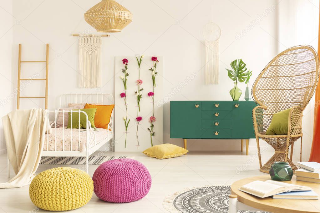 Colorful and stylish boho kid's bedroom with peacock chair, single metal bed and green wooden cabinet