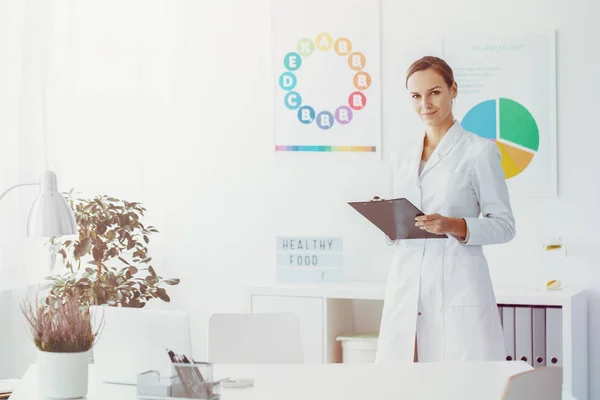 自信的医生站在她的办公室与丰富多彩的图表在背景 — 图库照片