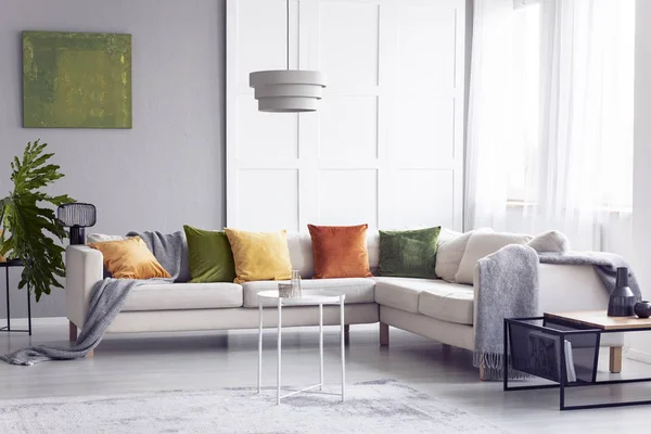 Lamp above table next to corner sofa with pillows in apartment interior with poster. Real photo