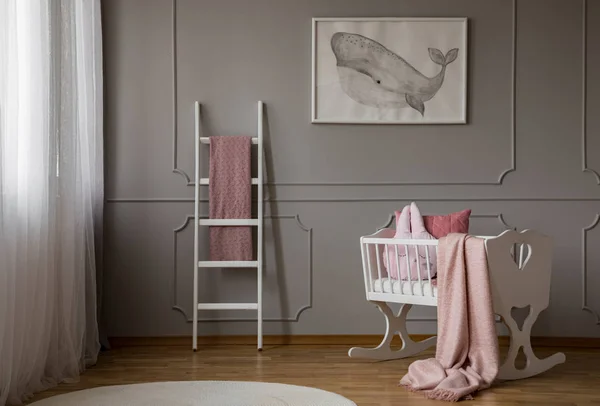 白色婴儿卧室内部的白色婴儿摇篮上的粉红毯子 配有海报和梯子 真实照片 — 图库照片