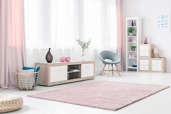 Bright living room interior with wooden cabinet, grey stylish chair and fluffy pastel pink rug
