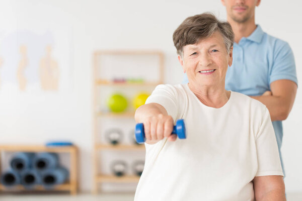Улыбающийся старший держит вес во время реабилитации
