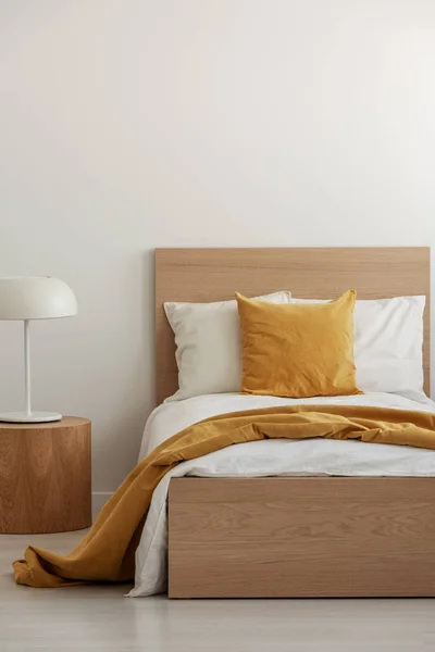 Yellow pillow and blanket on white bedding in simple hotel room with single bed, copy space on empty wall