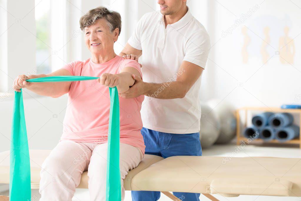 Senior exercising with a resistance band supported by a physiotherapist