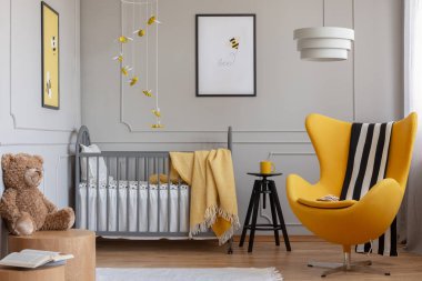 Siyah ve beyaz bir battaniye gri ahşap beşik beyaz yatak takımları ile yanındaki sarı koltuk var