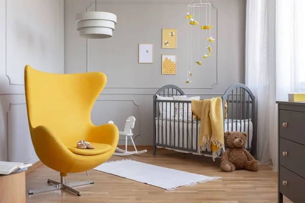 可爱的小鞋在时尚的黄色鸡蛋椅在可爱的婴儿房与灰色的木制婴儿床和蜜蜂口音 — 图库照片