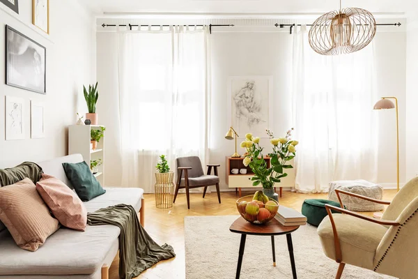 ソファと窓の明るいリビング ルーム インテリアの肘掛け椅子とテーブルの上の花 実際の写真 — ストック写真