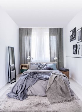 Sonraki pencerede perdeler ile beyaz yatak odası iç gri çarşaflı yatağa ayna. Gerçek fotoğraf