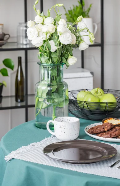 コーヒーのマグカップとダイニング テーブルの上の大きな皿の横にガラスの花瓶の白いバラ — ストック写真