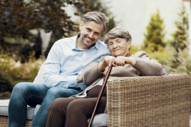 Oğlum ve annesi bir bahçede bir hasır kanepede oturan baston