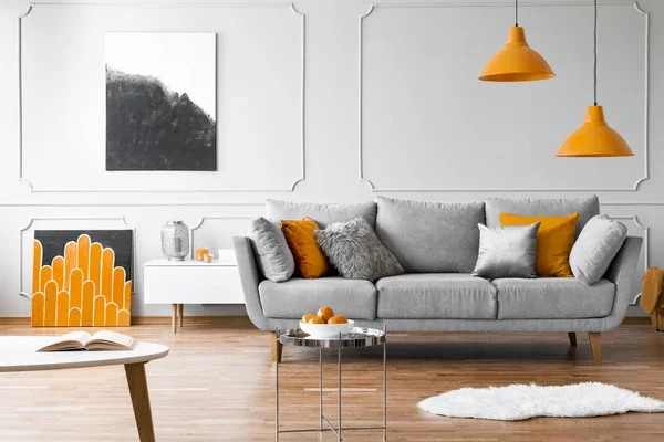 橙色灯在灰色沙发上方的客厅内部 有海报和银色的桌子 真实照片 — 图库照片