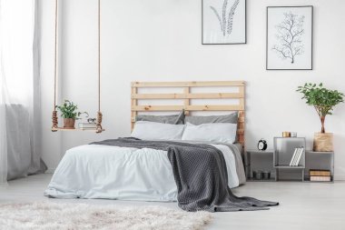 Kitap ve bitki yatak ile Ahşap karyola ve gri ve beyaz yatak yanında tencerede ile şık salıncak