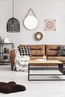 Battaniye ve aydınlık oturma odası iç limon suyu ve kitap ve ayna, saat ve duvardaki poster ile kahve masasıyla gerçek fotoğraf desenli yastıkları ile kahverengi deri kanepe