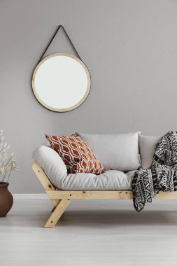 Desenli yastık ve çizgili battaniye, gerçek bir fotoğraf ile rahat kanepe ile parlak bej oturma odası duvar ahşap çerçeve içinde yuvarlak ayna