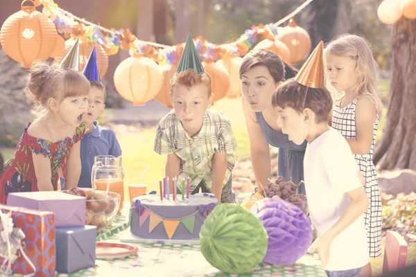 孩子们在生日聚会上用礼物和灯笼吹灭蛋糕上的蜡烛 — 图库照片