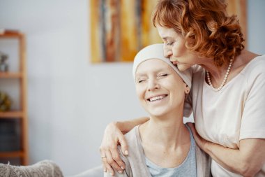 Senior redhead woman kissing forehead of her happy best friend suffering from cervical cancer clipart