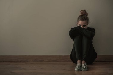 Katta, kopya alanı boş duvara oturan karanlık kıyafetlerle anksiyete bozukluğu olan genç kadın