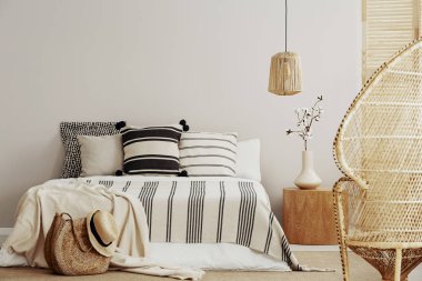 Ahşap Komidin, king size Yataklı çizgili yatak ve rattan tavus kuşu koltuk ile vazoda beyaz boş duvar alanı parlak şık yatak odası çiçek ile kopyalama
