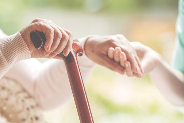 Closeup of senior lady holding walking stick in one hand and holding nurse's hand in the other