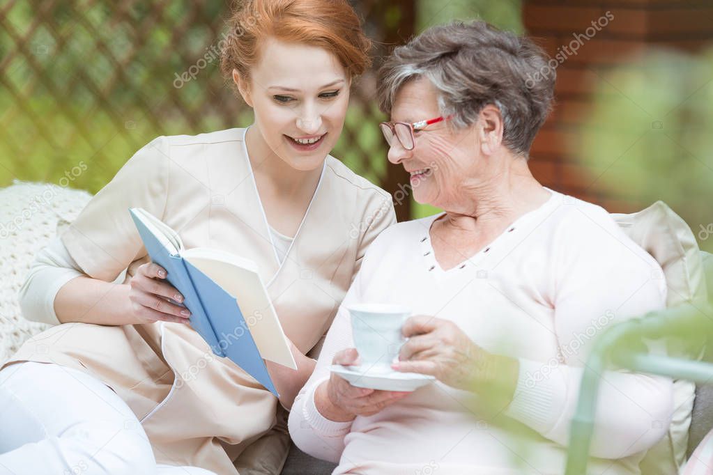 Beautiful redhead nurse shows photo album to senior lady in the garden