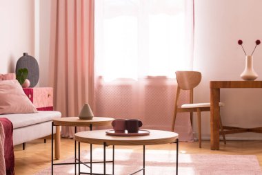 Şık pastel pembe oturma odasında ahşap kahve masasında iki kahve bardağı