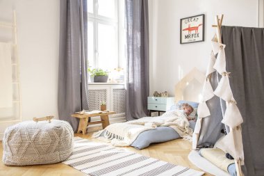 Mavi yatak üzerinde poster ile çocuğun yatak odası iç halı üzerinde pencere ve puf gri perdeler. Gerçek fotoğraf
