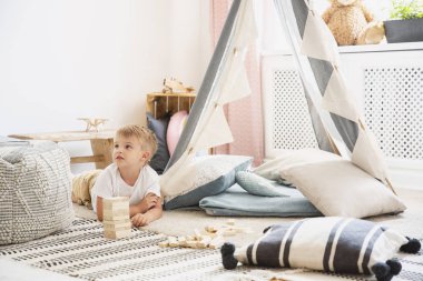 Şirin küçük çocuk rahat yastıklar ve desenli halı, kopya alanı ile gerçek fotoğraf ile gri çadır ile İskandinav oyun odası katında yatıyor