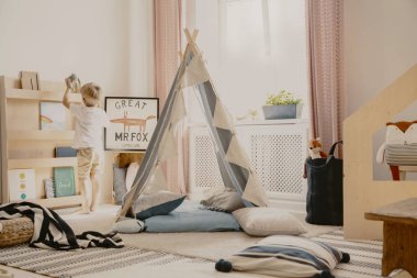 Cozy kid's room with pastel colored curtains and scandinavian tent with pillows, real photo
