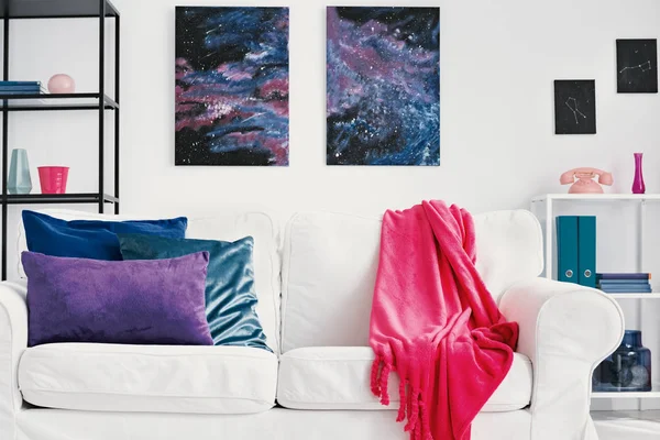 壁にギャラクシーグラフィックとスタイリッシュなリビングルームで 青色と緑色の枕と白いソファの上のピンクの毛布 — ストック写真