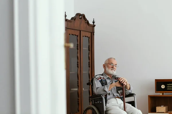 坐在轮椅上 用拐杖支撑自己的老人 — 图库照片