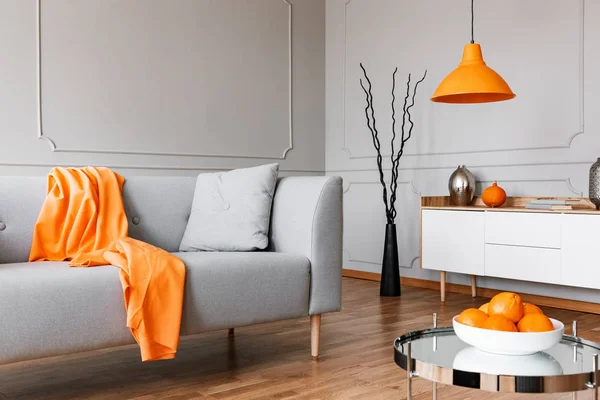 フラット インテリア ランプをキャビネットの上に銀のテーブルの横にある灰色の長いすにオレンジの毛布 実際の写真 — ストック写真