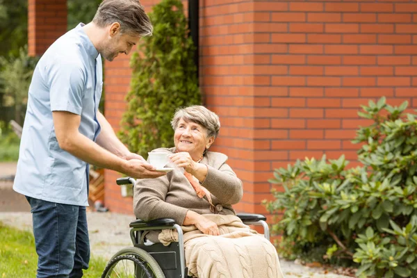 車椅子で彼の年長の患者にお茶を与えるオスの看護婦 — ストック写真