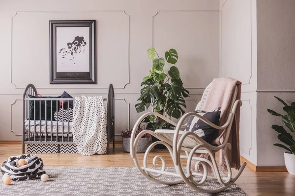 Качающее кресло и плакат в интерьере спальни серого ребенка с растением и одеялом на колыбели. Настоящее фото — стоковое фото