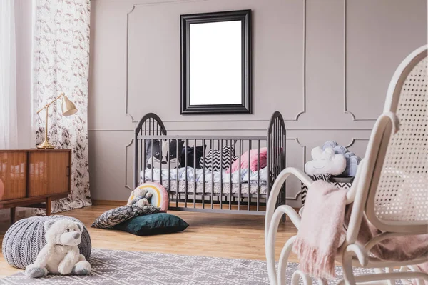 Ours en peluche blanc sur le sol de l'intérieur élégant de la chambre de bébé avec berceau en bois gris avec oreillers, fauteuil à bascule blanc et affiche maquette sur le mur — Photo