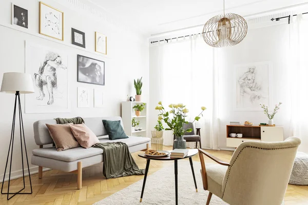 Mesa entre sillón y sofá gris en el interior de la sala de estar blanca con carteles. Foto real — Foto de Stock