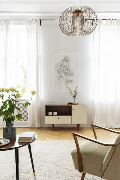 Flores sobre mesa junto a sillón bajo lámpara en luminoso salón interior con póster. Foto real — Foto de Stock