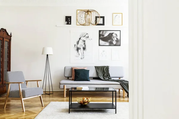 Tafel op tapijt naast de fauteuil in de woonkamer interieur met posters boven de grijze bank. Echte foto — Stockfoto