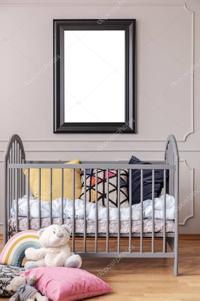 Mockup poster in black frame on the grey wall of baby room interior with crib with pillows, vertical view